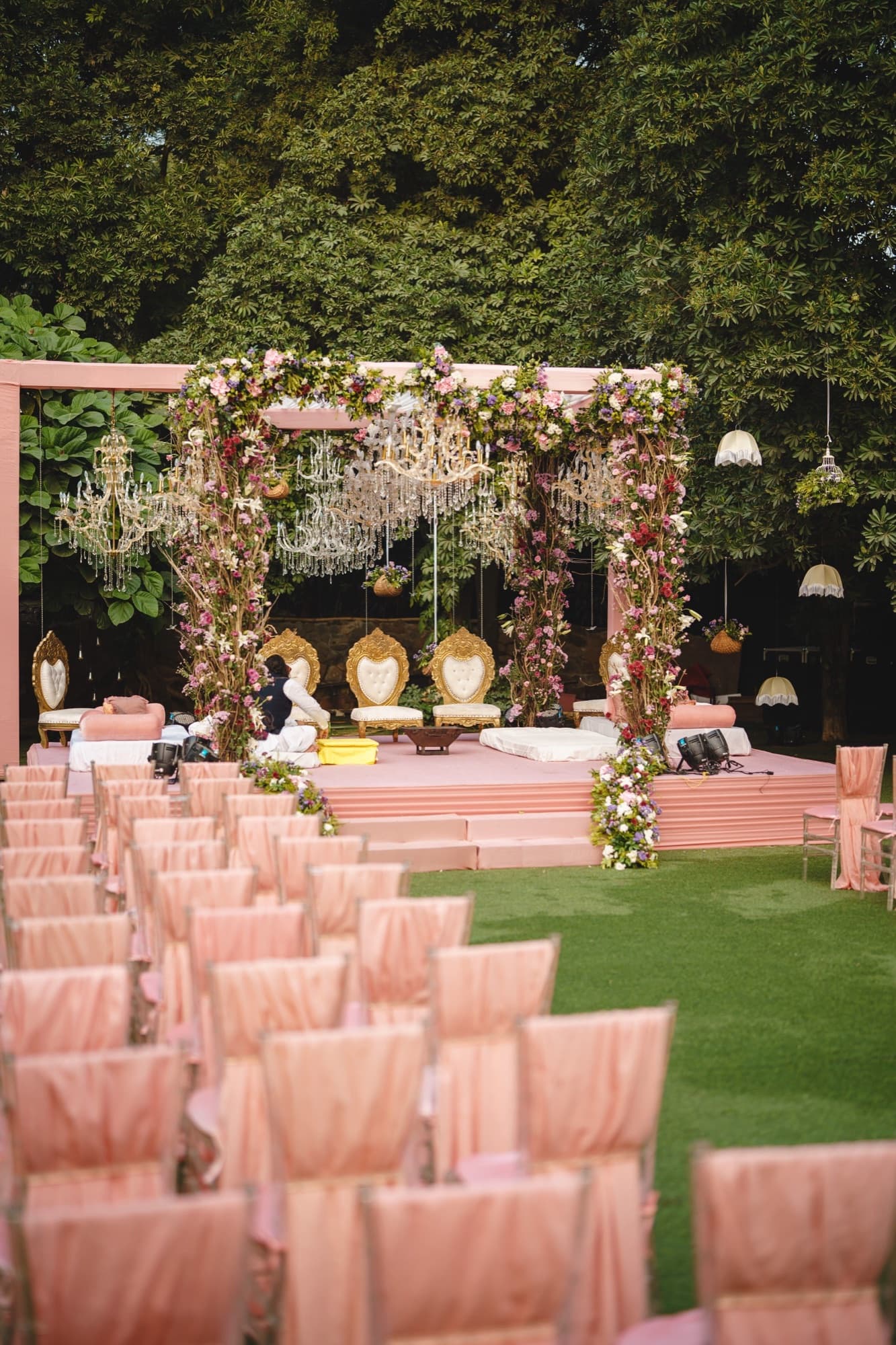 An outdoor wedding stage under trees, rows of draped chairs waiting for guests.